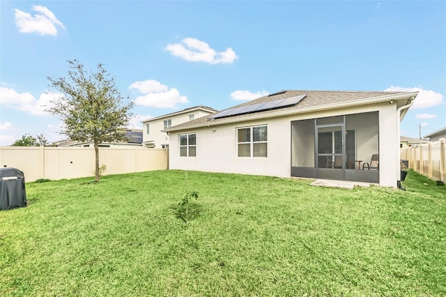 back of house featuring a lawn, a sunroom, and solar panels