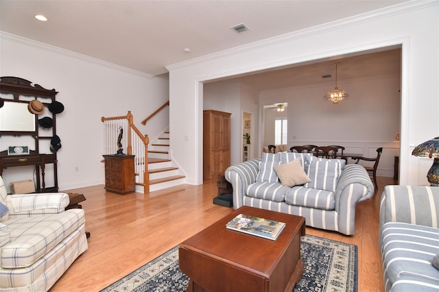 living room featuring a notable chandelier, ornamental molding, and light hardwood / wood-style flooring