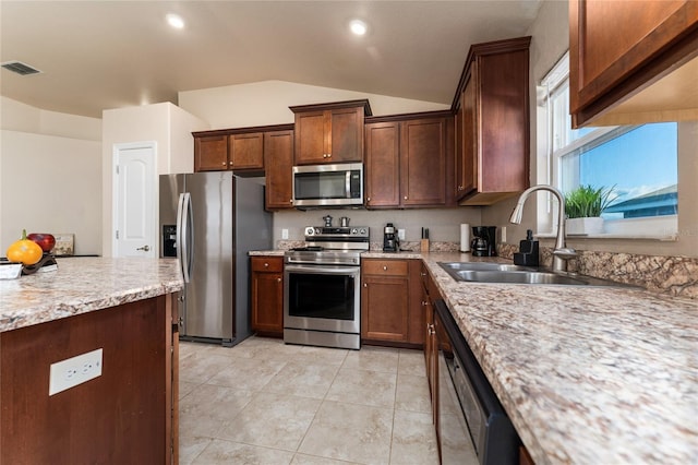 kitchen with appliances with stainless steel finishes, light stone counters, vaulted ceiling, sink, and light tile patterned floors