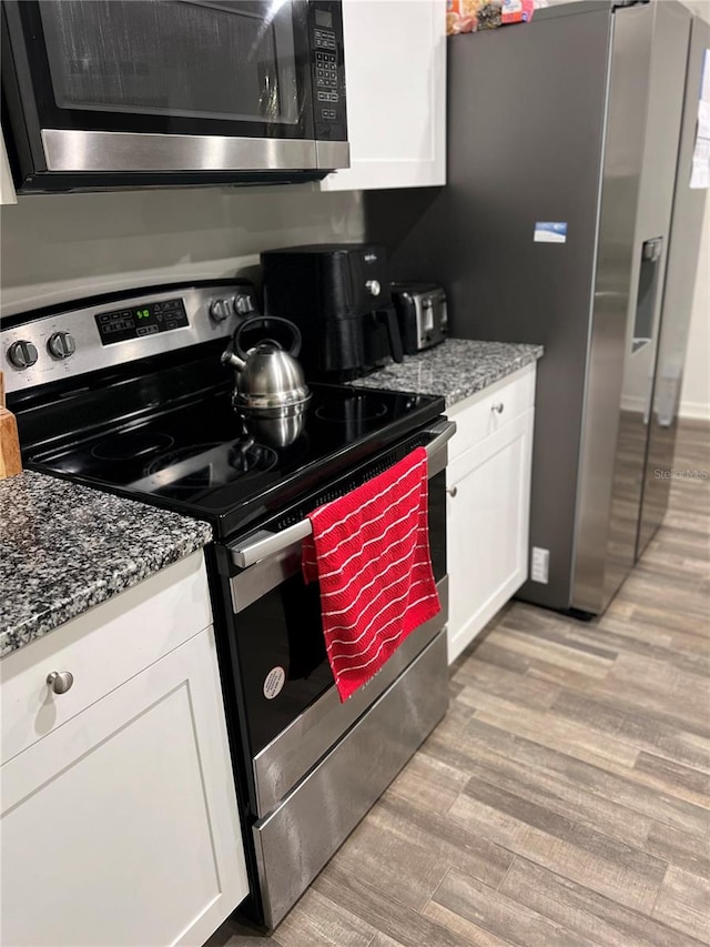 kitchen with white cabinets, stainless steel appliances, light hardwood / wood-style flooring, and stone counters