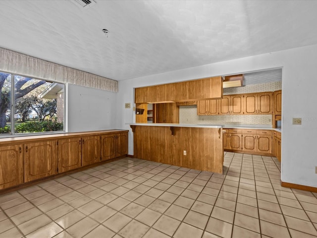 kitchen featuring kitchen peninsula, a kitchen breakfast bar, backsplash, and light tile patterned floors