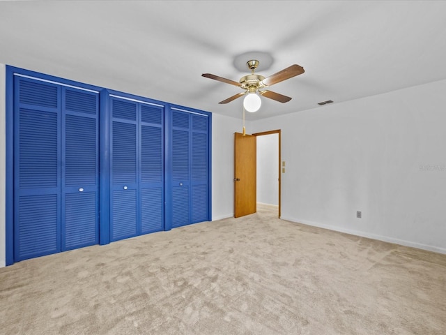 unfurnished bedroom featuring ceiling fan, light carpet, and multiple closets