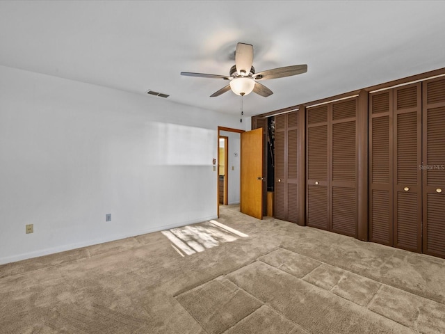 unfurnished bedroom with light carpet, ceiling fan, and multiple closets