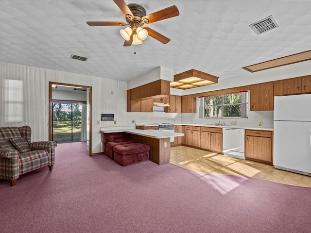 kitchen featuring a kitchen bar, light colored carpet, white appliances, and a wealth of natural light