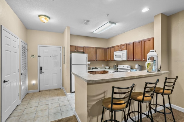 kitchen with kitchen peninsula, a breakfast bar, a textured ceiling, white appliances, and light tile patterned flooring