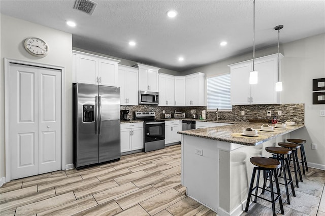 kitchen featuring white cabinets, hanging light fixtures, appliances with stainless steel finishes, kitchen peninsula, and a breakfast bar area