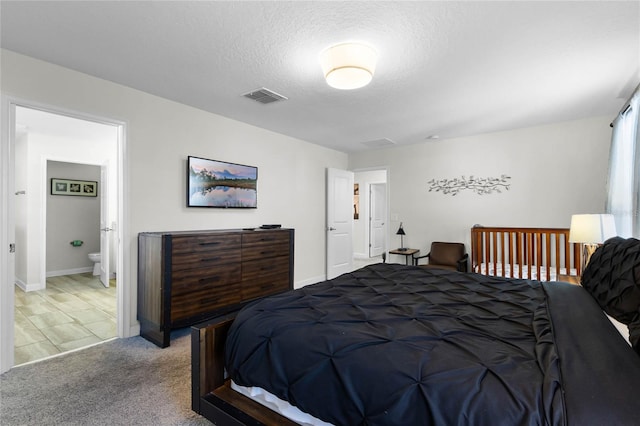 bedroom with ensuite bath, carpet, and a textured ceiling