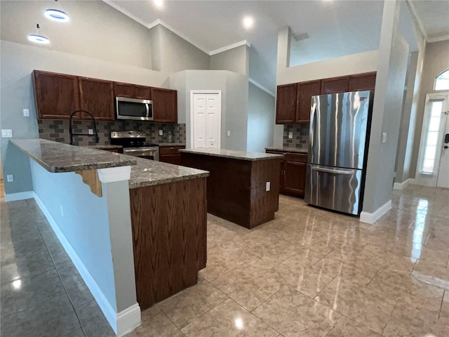 kitchen with a center island, a kitchen breakfast bar, high vaulted ceiling, crown molding, and appliances with stainless steel finishes