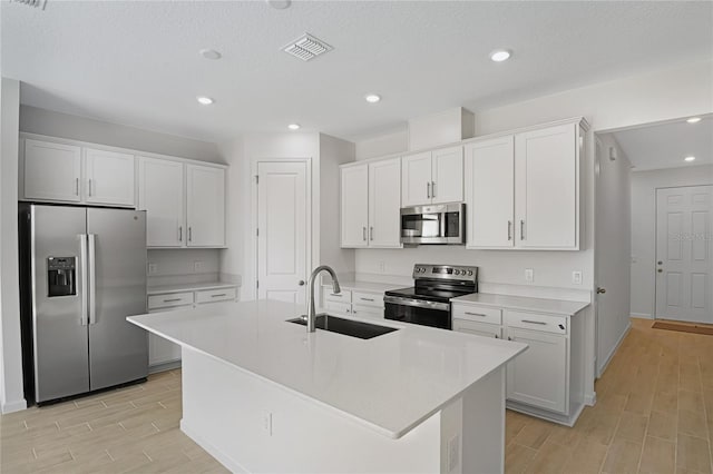 kitchen featuring appliances with stainless steel finishes, sink, white cabinetry, a textured ceiling, and an island with sink