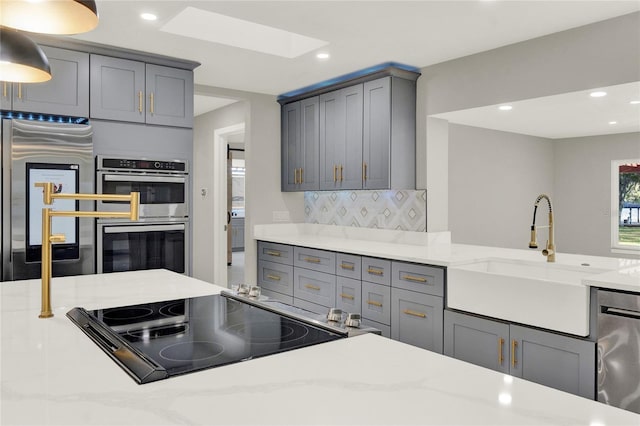 kitchen with light stone countertops, a skylight, stainless steel appliances, sink, and gray cabinets