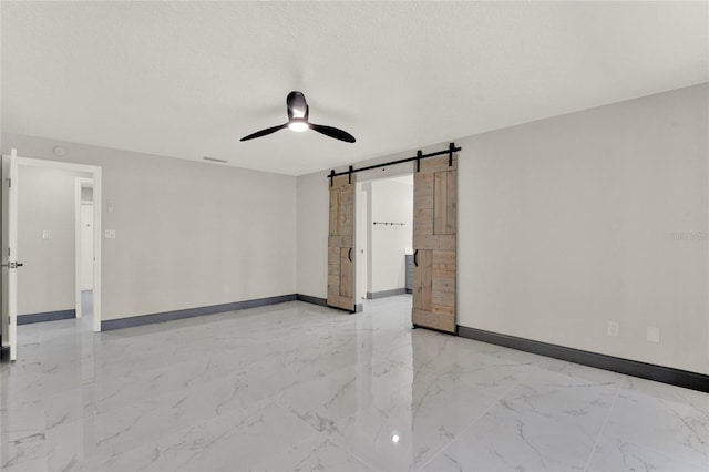 empty room featuring ceiling fan, a barn door, and a textured ceiling