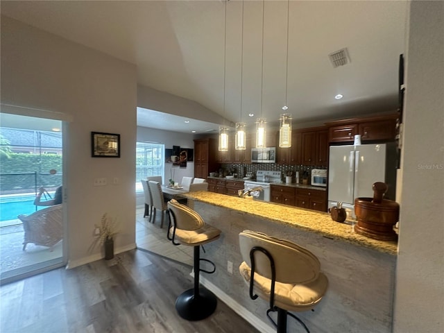 kitchen with decorative light fixtures, white appliances, a wealth of natural light, and lofted ceiling