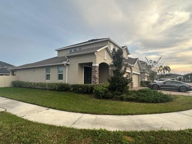 view of side of property with stucco siding, an attached garage, driveway, and a yard