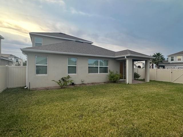 rear view of property featuring stucco siding, a lawn, a fenced backyard, and a shingled roof