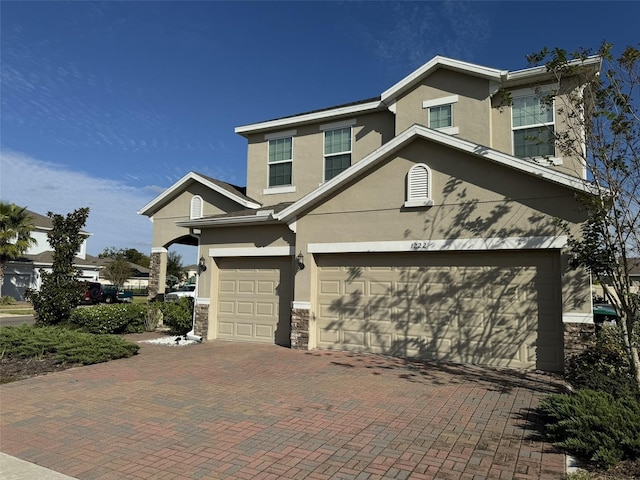 view of front of house with decorative driveway, an attached garage, stone siding, and stucco siding