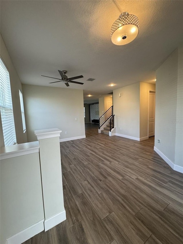 unfurnished living room featuring a textured ceiling, ceiling fan, and dark wood-type flooring