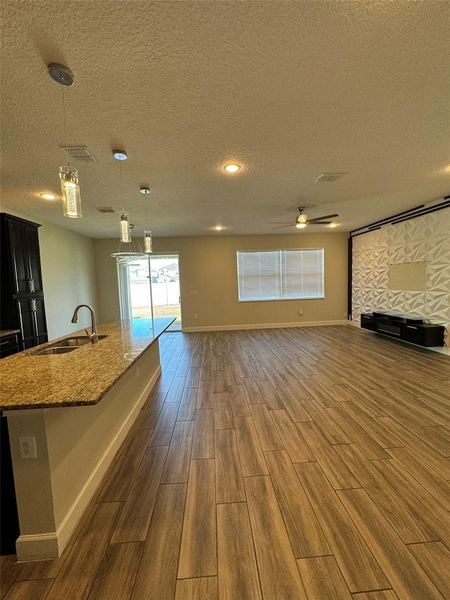 unfurnished living room with ceiling fan with notable chandelier, a textured ceiling, dark wood-type flooring, and sink