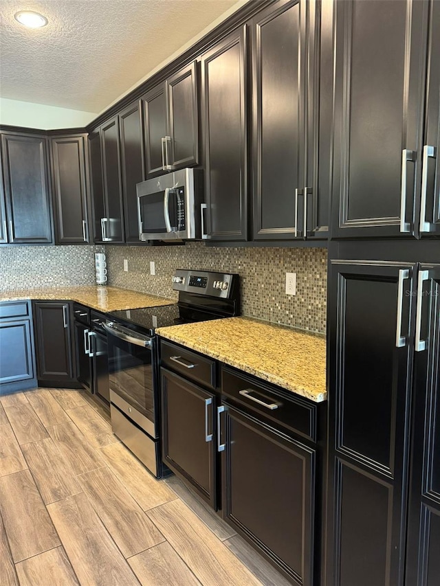 kitchen featuring decorative backsplash, appliances with stainless steel finishes, a textured ceiling, and light hardwood / wood-style flooring