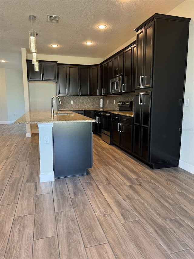 kitchen with a center island with sink, light wood-type flooring, hanging light fixtures, and appliances with stainless steel finishes