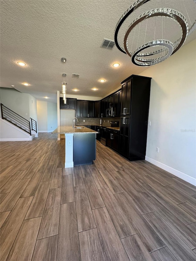 kitchen featuring pendant lighting, a textured ceiling, hardwood / wood-style flooring, and an island with sink