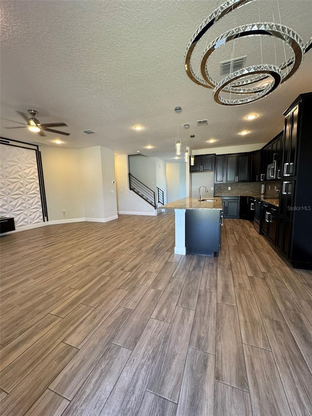 kitchen featuring pendant lighting, a center island with sink, sink, hardwood / wood-style flooring, and a textured ceiling