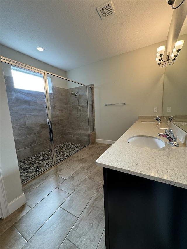 bathroom featuring an inviting chandelier, vanity, a textured ceiling, and tiled shower