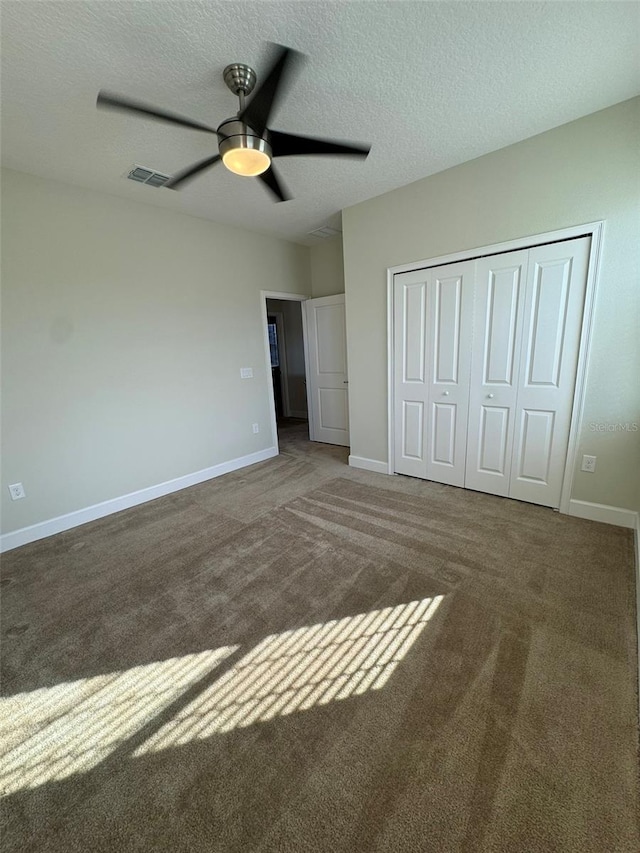 unfurnished bedroom with a textured ceiling, a closet, dark carpet, and ceiling fan