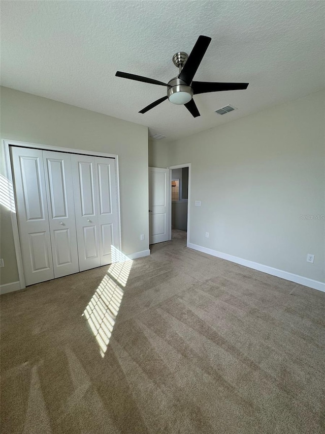 unfurnished bedroom with ceiling fan, light colored carpet, a textured ceiling, and a closet