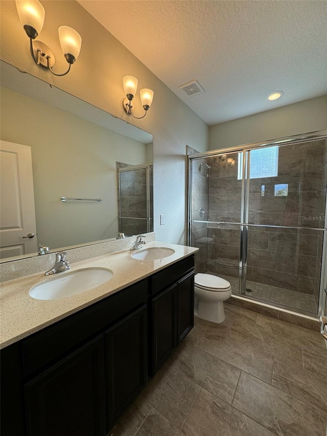 bathroom with a textured ceiling, vanity, toilet, and walk in shower