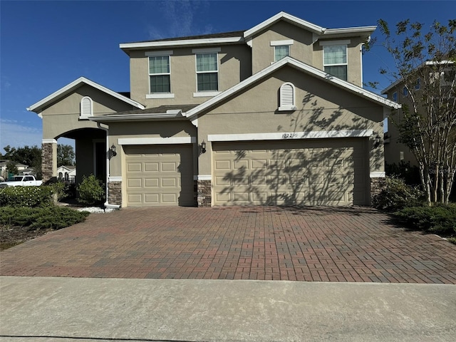 view of front of home featuring decorative driveway, a garage, stone siding, and stucco siding