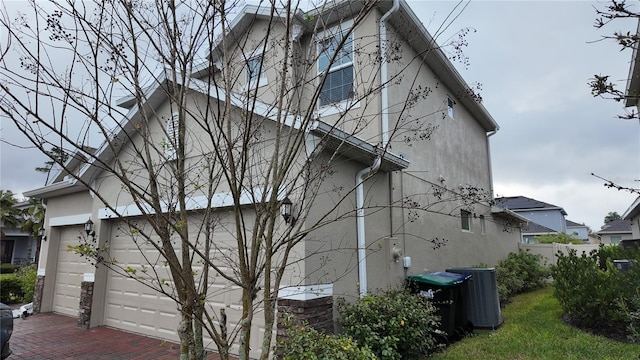 view of home's exterior featuring central air condition unit, stucco siding, decorative driveway, and a garage