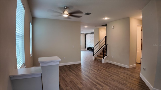 empty room with stairs, dark wood-type flooring, a ceiling fan, and visible vents