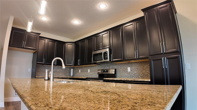 kitchen with an island with sink, a sink, appliances with stainless steel finishes, decorative backsplash, and light stone countertops