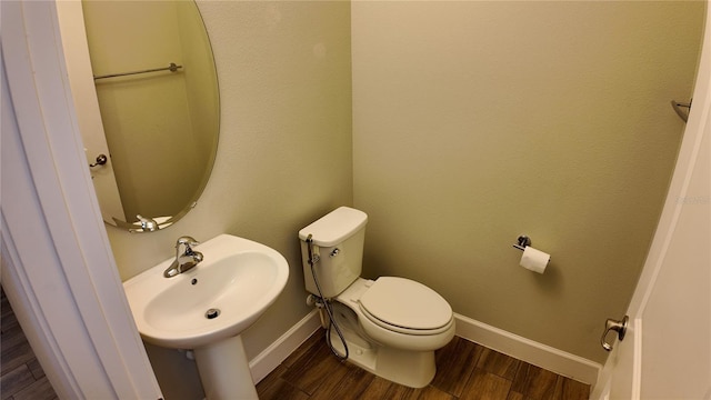 half bathroom with a sink, baseboards, toilet, and wood finished floors