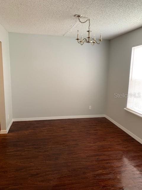 spare room with a chandelier, a textured ceiling, and dark hardwood / wood-style floors