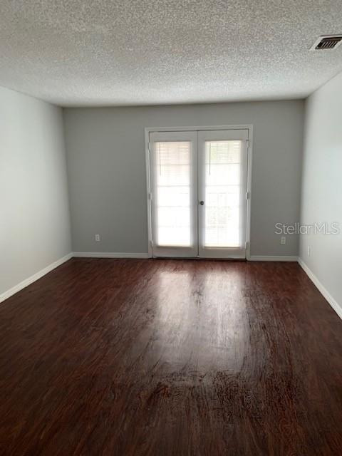 empty room featuring a textured ceiling, french doors, and dark hardwood / wood-style floors