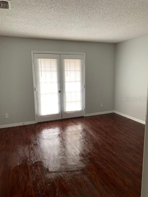 spare room with french doors, a textured ceiling, and dark wood-type flooring