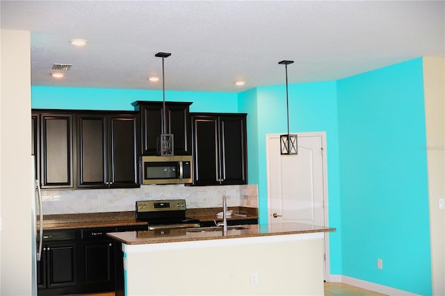 kitchen featuring sink, decorative backsplash, an island with sink, appliances with stainless steel finishes, and decorative light fixtures