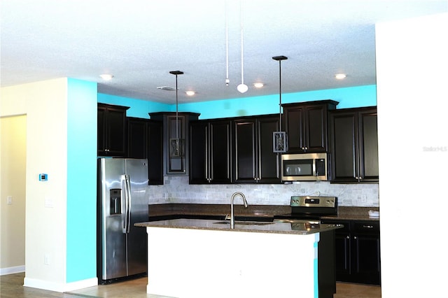 kitchen featuring sink, hanging light fixtures, backsplash, an island with sink, and appliances with stainless steel finishes