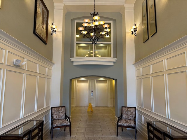 interior space featuring crown molding, a notable chandelier, a towering ceiling, and tile patterned floors