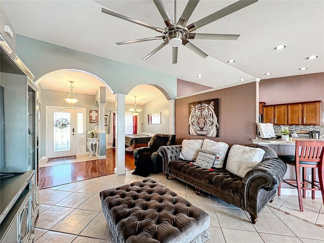 tiled living room with a textured ceiling, ornate columns, vaulted ceiling, and ceiling fan with notable chandelier