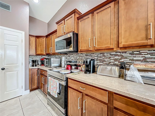 kitchen with light tile patterned flooring, tasteful backsplash, appliances with stainless steel finishes, and vaulted ceiling