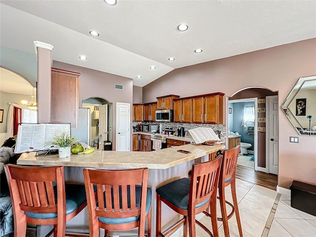 kitchen with stainless steel appliances, kitchen peninsula, vaulted ceiling, a breakfast bar, and light tile patterned flooring