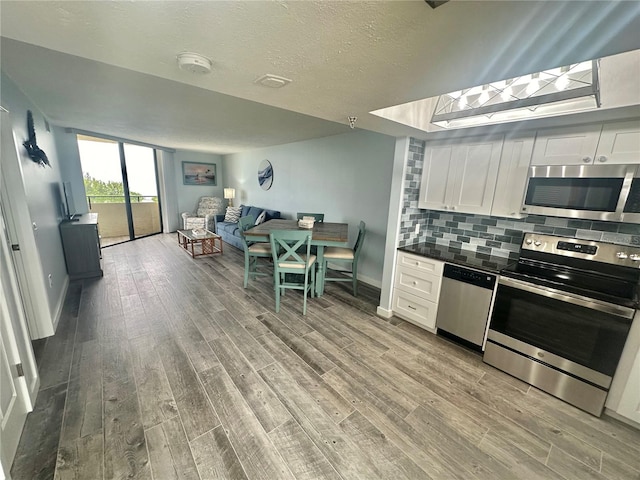 kitchen with light wood-type flooring, a textured ceiling, tasteful backsplash, white cabinetry, and stainless steel appliances