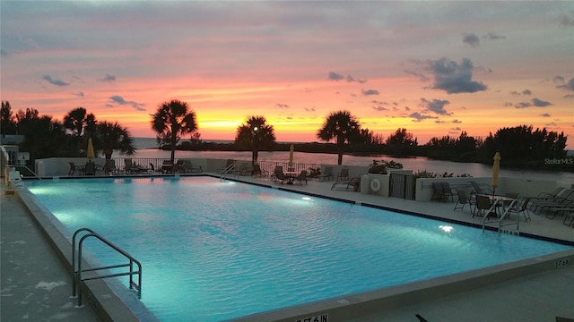 pool at dusk with a water view and a patio