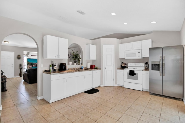 kitchen with white appliances, white cabinets, vaulted ceiling, light tile patterned floors, and light stone counters