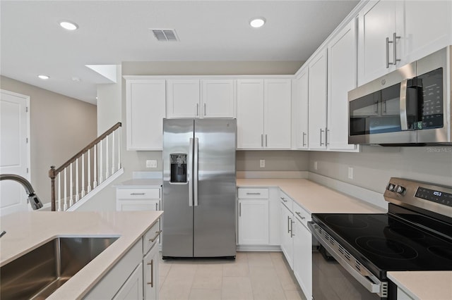 kitchen with appliances with stainless steel finishes, light tile patterned floors, white cabinetry, and sink