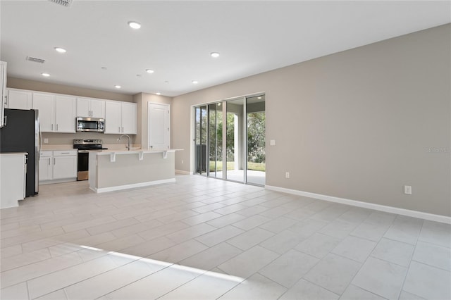 kitchen featuring a breakfast bar, stainless steel appliances, light tile patterned floors, white cabinets, and an island with sink