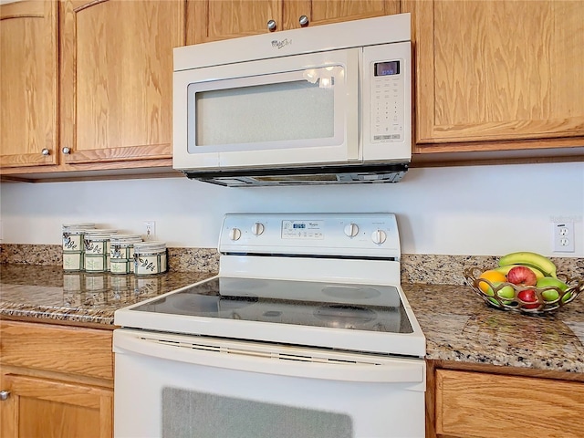 kitchen featuring white appliances and dark stone countertops