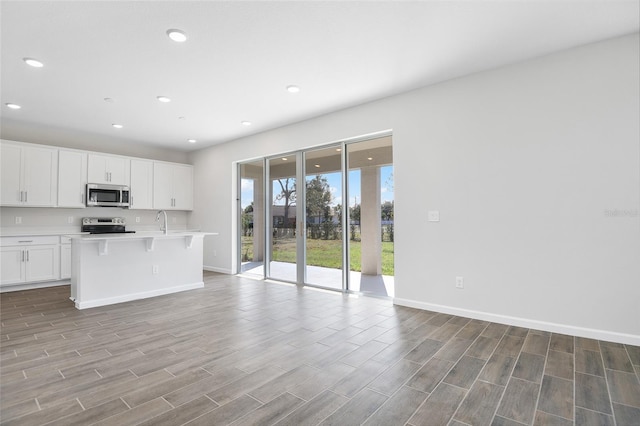 kitchen with sink, a breakfast bar area, white cabinetry, stainless steel appliances, and a kitchen island with sink